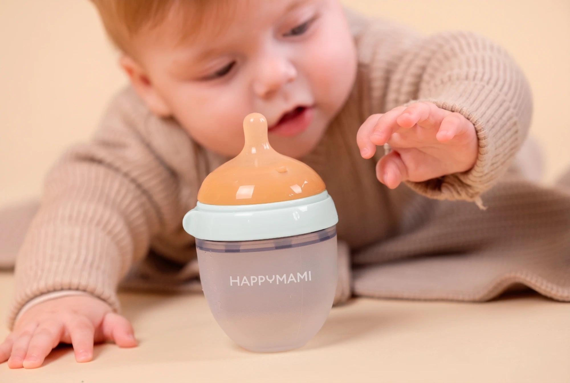 Baby looking curiously at a Happymami bottle and reaching a hand out toward it