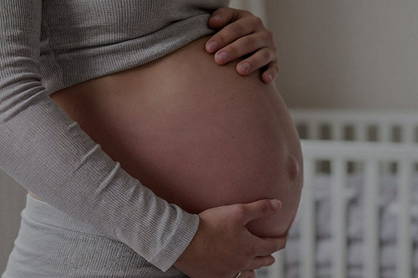 Mujer embarazada sujetando su barriga junto a una cuna