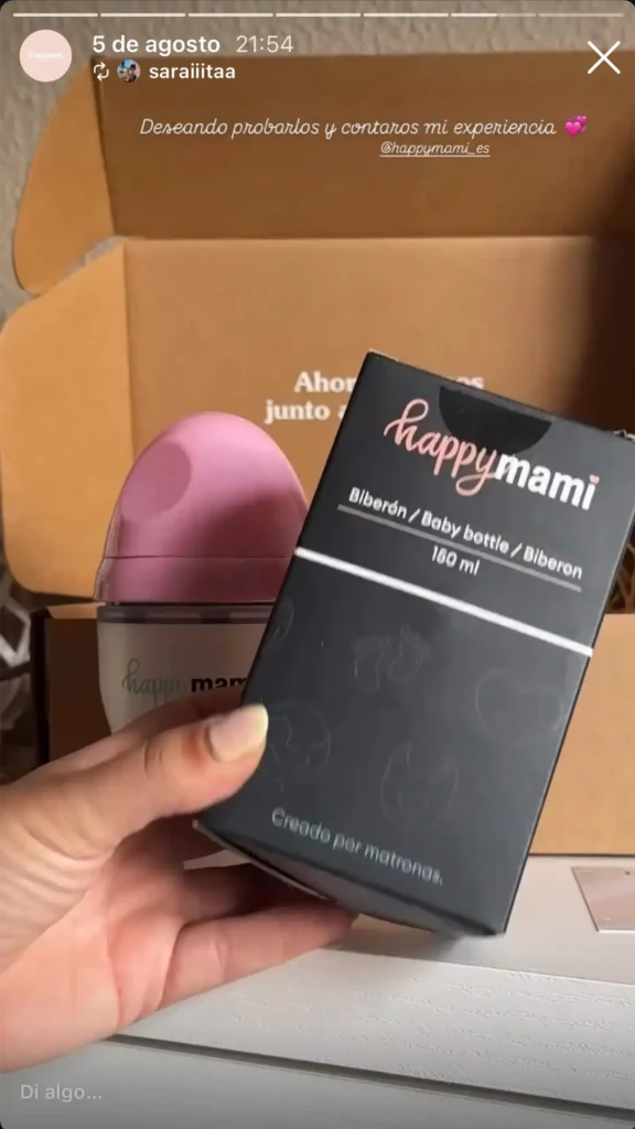 Mano sosteniendo la caja negra del biberón Happymami de 180 ml junto a un biberón rosa en su caja abierta